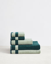 A stack of Bed Threads’ Forest & Sage Two-Toned 100% Cotton Terry Bath Sheet Bundle, arranged from largest to smallest, sits against a white wall on a light surface. - view
