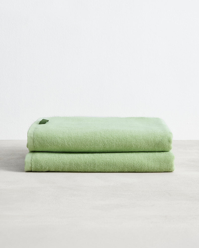 A set of two neatly folded Apple 100% Cotton Terry Bath Sheets by Bed Threads is shown on a light gray surface against a plain white background, each featuring a small tag.