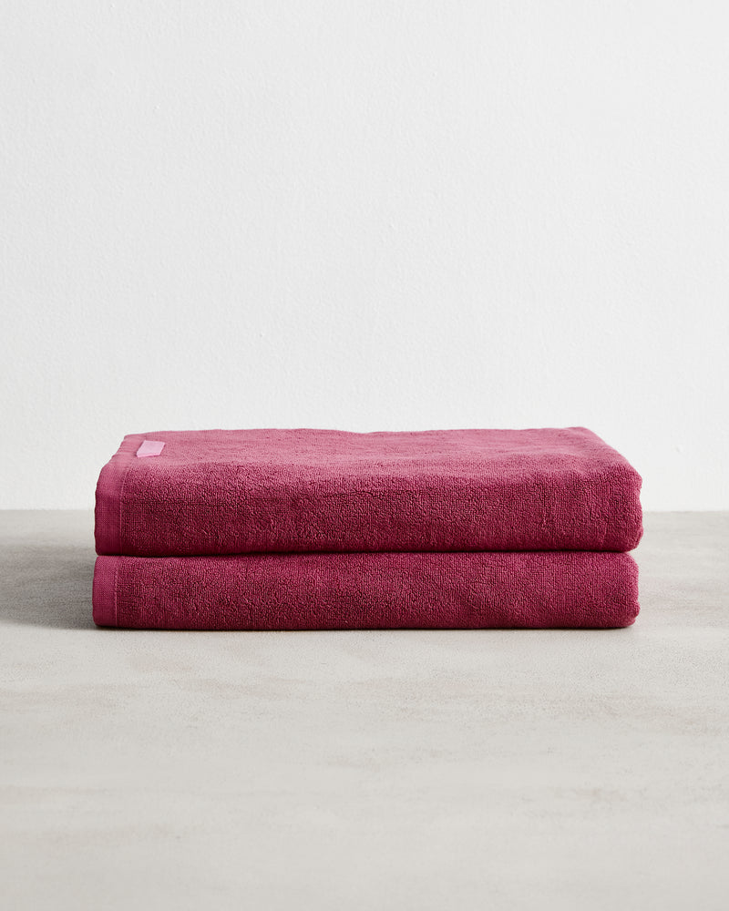 Two neatly folded Berry 100% Cotton Terry Bath Sheets by Bed Threads, stacked on a light textured surface with a white background, offering softness and high absorbency. Set of two.