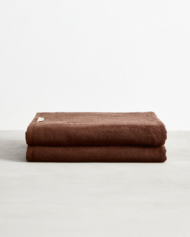 Two Espresso 100% Cotton Terry Bath Sheets by Bed Threads, neatly folded and stacked on a light gray surface against a plain white background. Set of two.