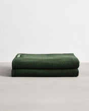 Two Moss 100% Cotton Terry Bath Sheets by Bed Threads are neatly folded and stacked on a light surface with a plain white background. - view