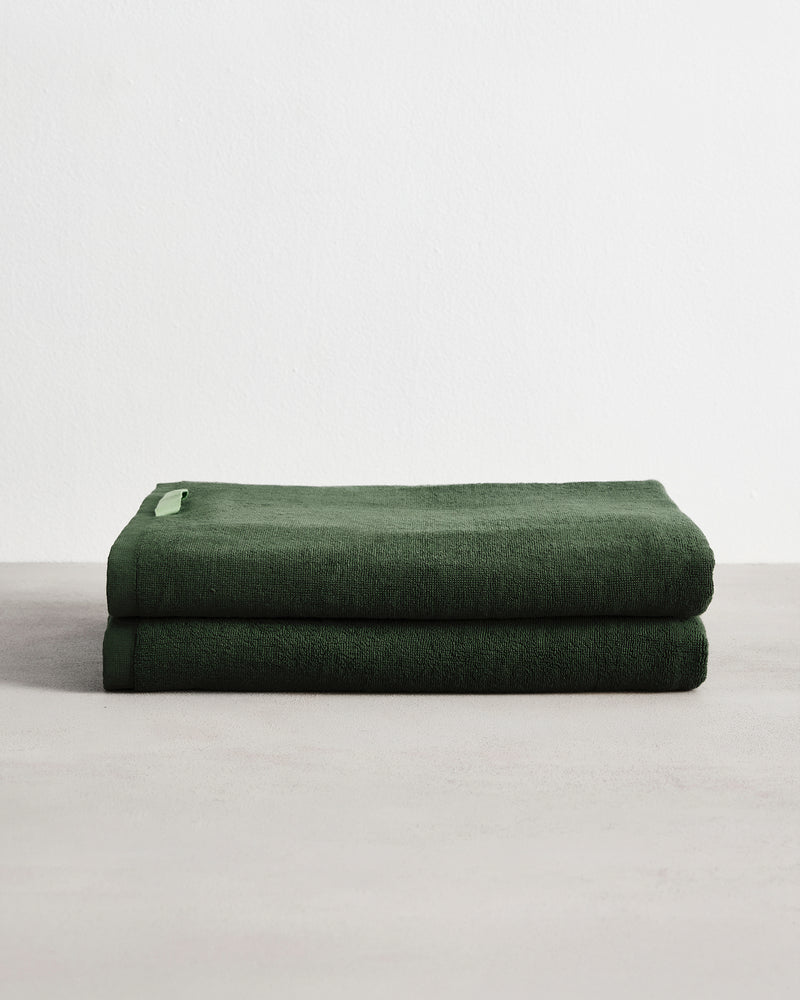 Two Moss 100% Cotton Terry Bath Sheets by Bed Threads are neatly folded and stacked on a light surface with a plain white background.