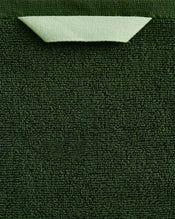 A close-up of the Bed Threads Moss 100% Cotton Terry Bath Towel Bundle shows its dark green textured surface, with a light green corner folded over to reveal the smooth backside and contrast with the highly absorbent terry fabric. - view