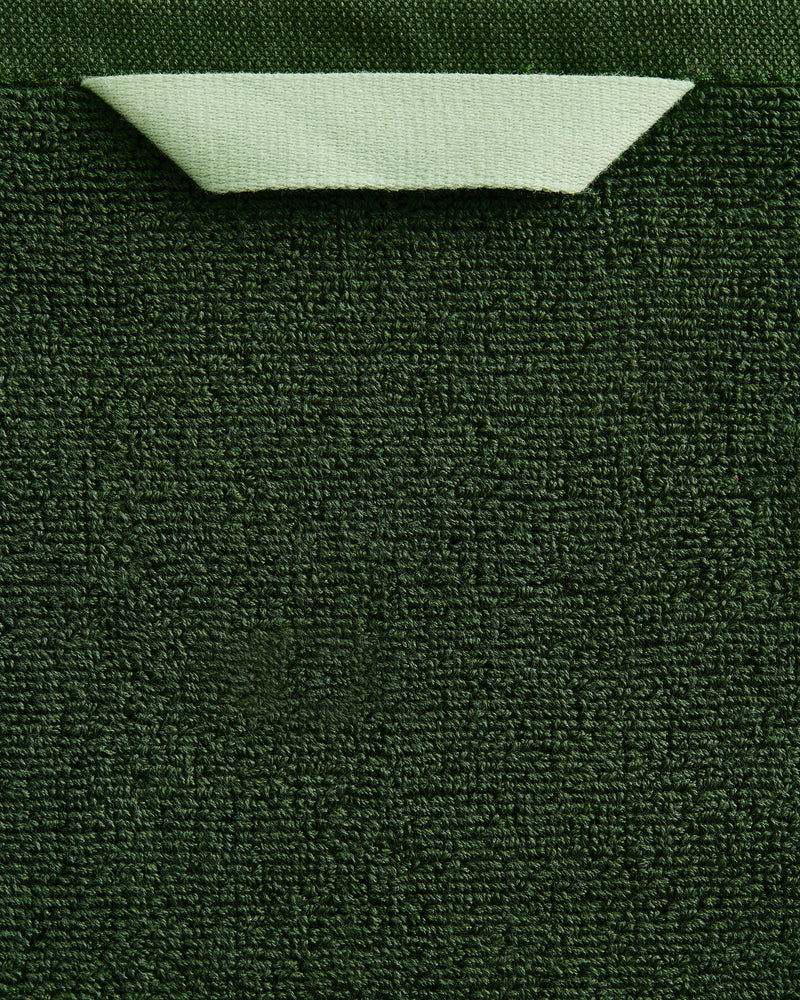 A close-up of the Bed Threads Moss 100% Cotton Terry Bath Towel Bundle shows its dark green textured surface, with a light green corner folded over to reveal the smooth backside and contrast with the highly absorbent terry fabric.