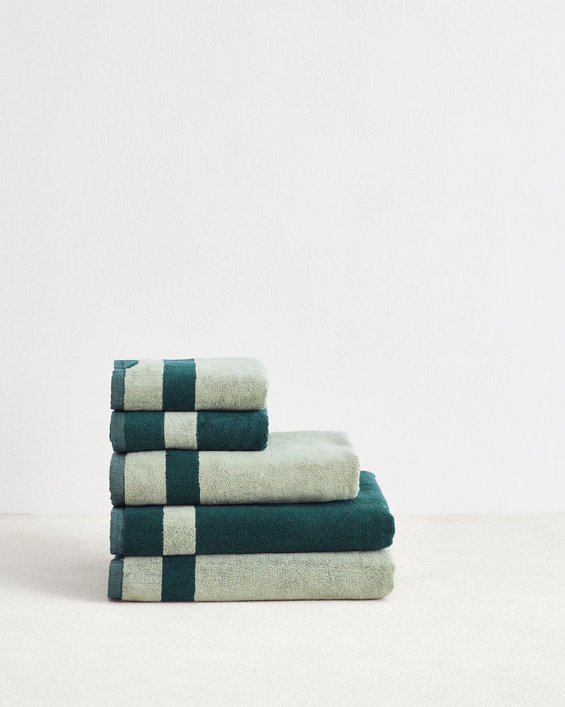 A neatly folded stack of four Forest & Sage Two-Toned 100% Cotton Terry Bath Towels by Bed Threads, arranged from largest to smallest, sits on a light surface with a white background.