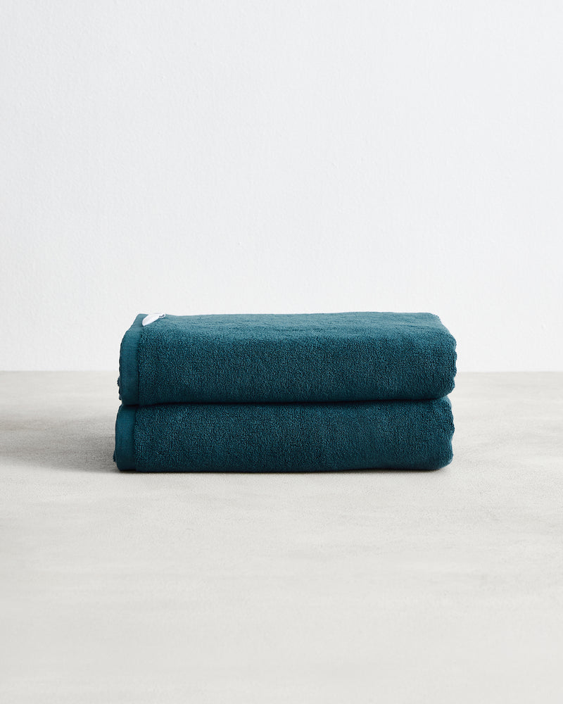 A set of two Aegean 100% Cotton Terry Bath Towels by Bed Threads rests folded on a light gray surface against a white background, highlighting their plush, highly absorbent texture.