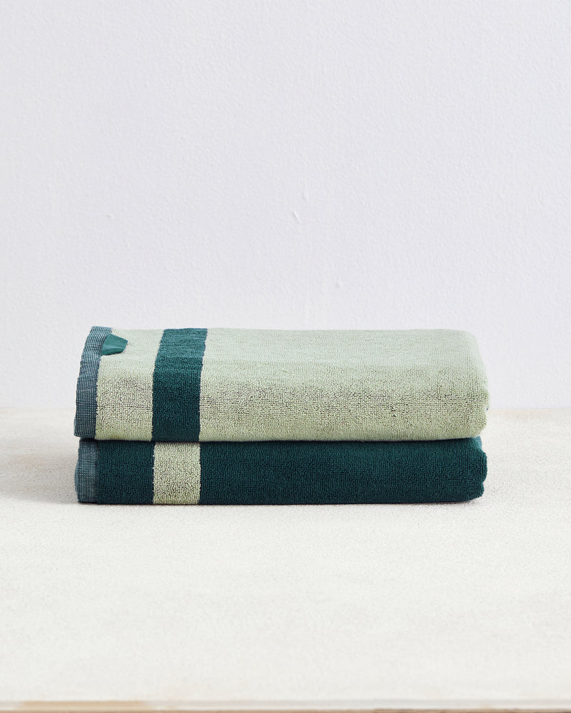 The Bed Threads Forest & Sage Two-Toned 100% Cotton Terry Bath Towels (Set of Two) are neatly folded and stacked on a light beige surface with a plain white background.