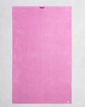The Bed Threads Bubblegum 100% Cotton Terry Bath Sheet is a large, rectangular pink towel with plush, quick-drying fabric, a small loop at the top edge, and a beige tag at the bottom right corner, laid flat on a light background. - view