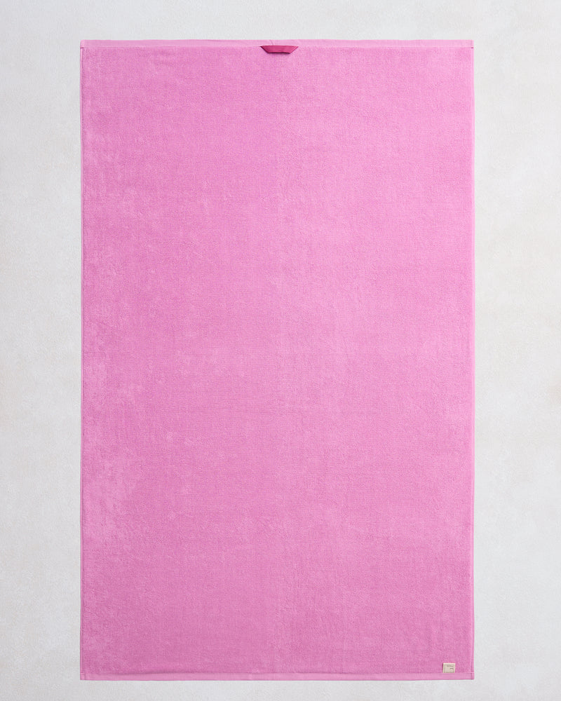 The Bed Threads Bubblegum 100% Cotton Terry Bath Sheet is a large, rectangular pink towel with plush, quick-drying fabric, a small loop at the top edge, and a beige tag at the bottom right corner, laid flat on a light background.