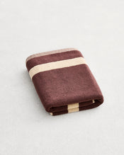 A folded cotton terry bath mat on a grey background, in a cacao colourway with an creme border. - view