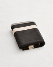 A folded cotton terry bath mat on a grey background, in a charcoal colourway with an oatmeal border. - view