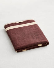 A folded cotton terry bath sheet on a grey background, in a cacao colourway with an creme border. - view