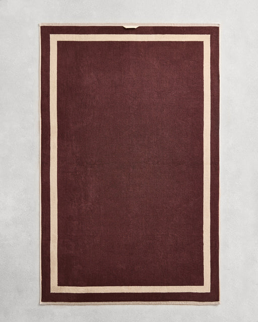 Flat cotton terry bath sheet on a grey background in a cacao colour with a ceme border.