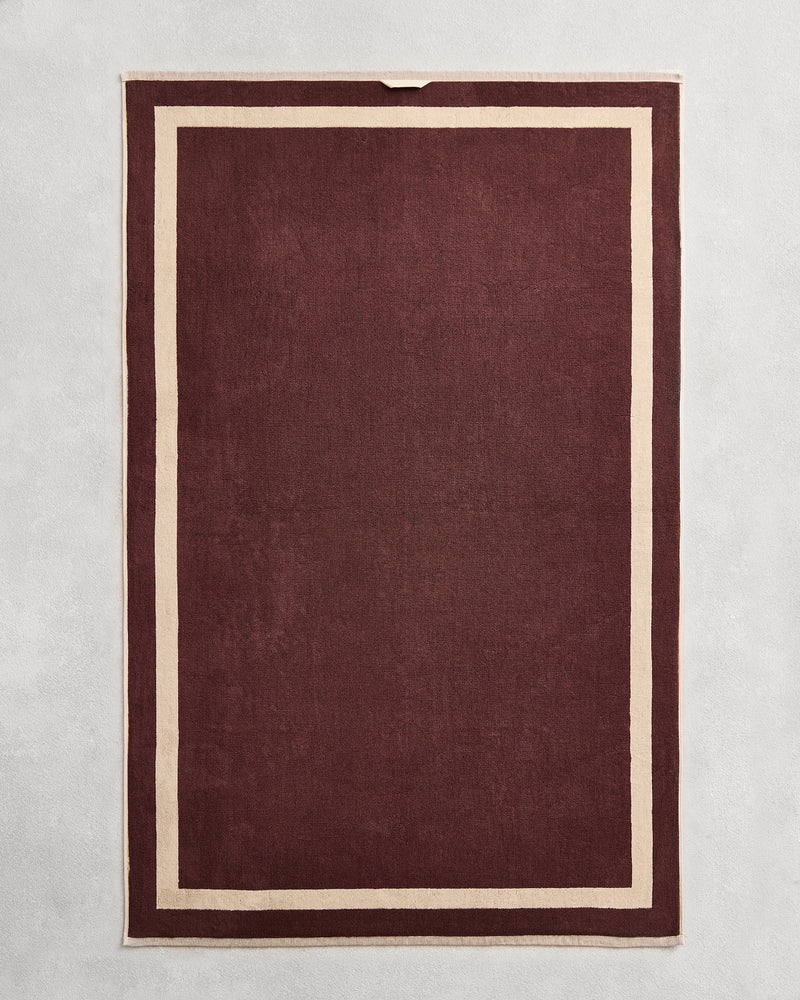 Flat cotton terry bath sheet on a grey background in a cacao colour with a ceme border.