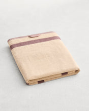 A folded cotton terry bath sheet on a grey background, in a creme colourway with a lavender border. - view