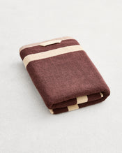 A folded cotton terry bath towel on a grey background, in a cacao colourway with an creme border. - view