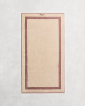 Flat cotton terry bath towel on a grey background in a creme colour with a lavender border. - view