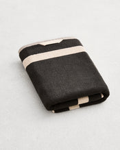 A folded cotton terry bath towel on a grey background, in a charcoal colourway with an oatmeal border. - view