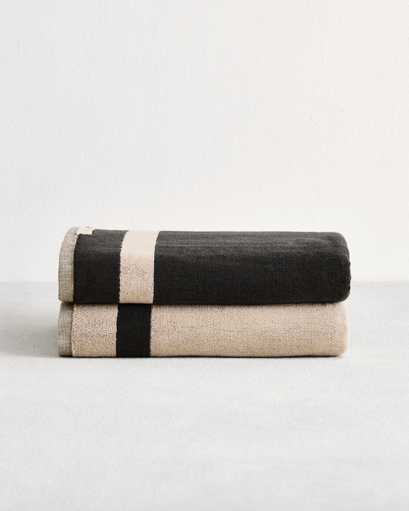 Stack of two cotton terry bath towels in reversible colours oatmeal and charcoal.