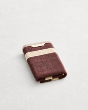 A folded cotton terry hand towel on a grey background, in a cacao colourway with a creme border. - view