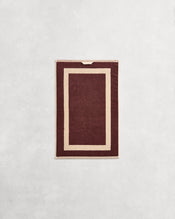 Flat cotton terry hand towel on a grey background in a cacao colour with a creme border. - view