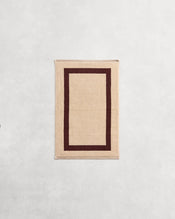 Flat cotton terry hand towel on a grey background in a creme colour with a cacao border. - view