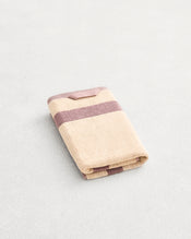 A folded cotton terry hand towel on a grey background, in a creme colourway with a lavender border. - view