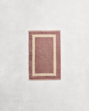 Flat cotton terry hand towel on a grey background in a lavender colour with a creme border. - view
