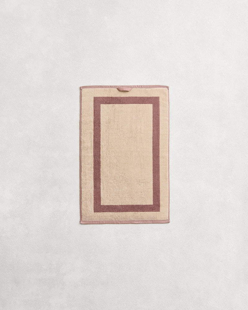 Flat cotton terry hand towel on a grey background in a creme colour with a lavender border.