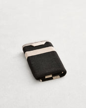 A folded cotton terry hand towel on a grey background, in a charcoal colourway with an oatmeal border. - view