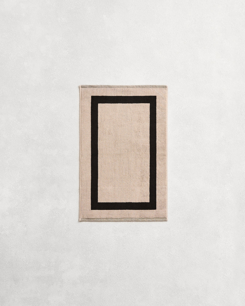 Flat cotton terry hand towel on a grey background in an oatmeal colour with a charcoal border.