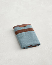 A neatly folded Bed Threads Cacao & Lagoon Two-Toned 100% Cotton Terry Hand Towel with two horizontal brown stripes rests on a light textured surface. - view