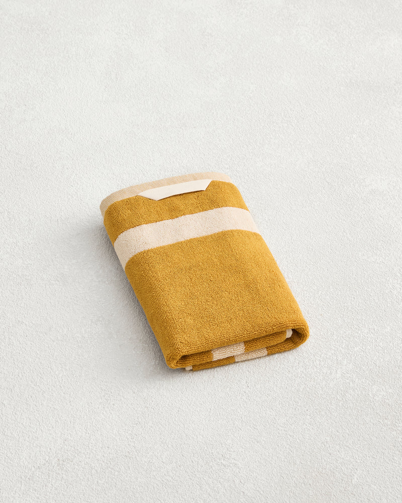 The Bed Threads Crème & Turmeric Two-Toned 100% Cotton Terry Hand Towel, crafted from plush 650GSM terry, is neatly folded and rests on a light textured surface.