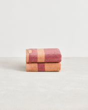 A neatly folded set of two Bed Threads Terracotta & Pink Clay Two-Toned 100% Cotton Terry Hand Towels is stacked on a smooth surface, displaying wide stripes in soft hues against a plain white background. - view