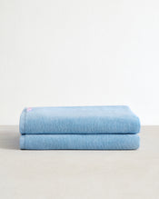 A set of two Sky 100% Cotton Terry Bath Sheets from Bed Threads are neatly folded and stacked on a light beige surface, set against a plain white background. - view