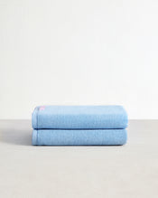 Two Sky 100% Cotton Terry Bath Towels by Bed Threads are neatly stacked, showcasing their high absorbency and light blue color against a plain white background. - view