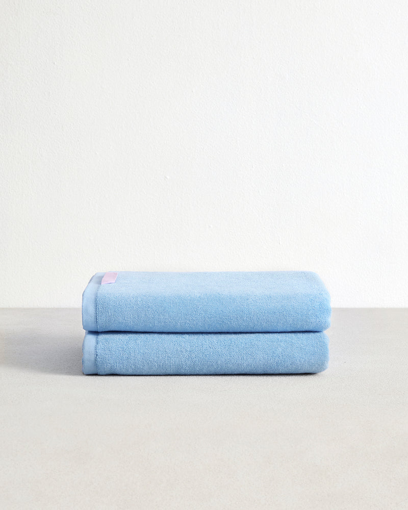 Two Sky 100% Cotton Terry Bath Towels by Bed Threads are neatly stacked, showcasing their high absorbency and light blue color against a plain white background.