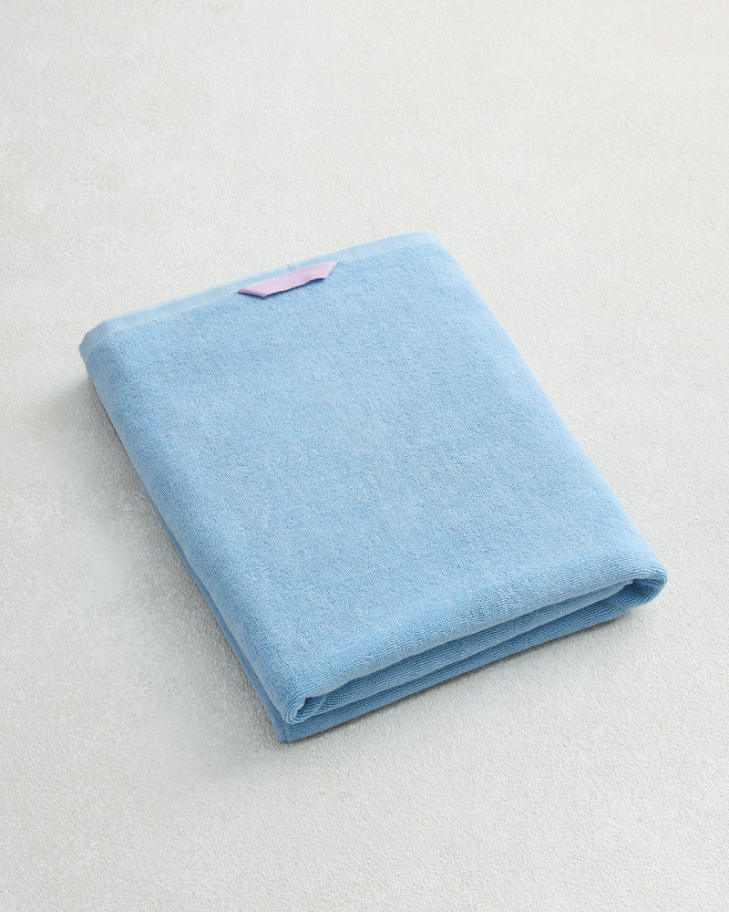 The Bed Threads Sky 100% Cotton Terry Bath Sheet, folded neatly with a small pink label, rests on a light, textured surface.