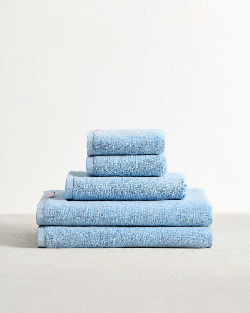 A neatly folded stack of Bed Threads Sky 100% Cotton Terry Bath Sheet Bundle is arranged on a light surface against a plain white background, showcasing bath sheets and towels in various sizes.