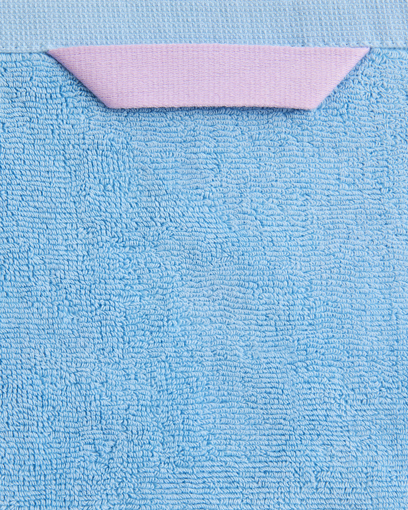 A close-up of Bed Threads’ Sky 100% Cotton Terry Bath Towels (Set of Two), highly absorbent and plush, featuring a pink triangular fabric loop, displayed against a light blue background.