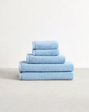 The Bed Threads Sky 100% Cotton Terry Bath Towel Bundle features five highly absorbent, light blue towels in assorted sizes, neatly stacked on a light surface against a plain white background. - view