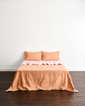 A neatly made bed with a peach-colored quilt cover in Terracotta & Rosewater, with two matching pillowcases in Terracotta, set against a plain white wall and dark wood floor. - view