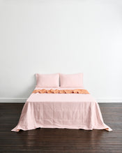 A neatly made bed with a light pink quilt cover in Terracotta & Rosewater with two matching pillowcases in Rosewater set against a plain white wall and dark wood floor. - view