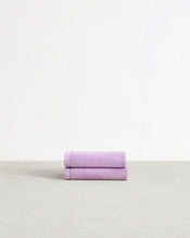 A set of two Bed Threads Violet 100% Cotton Terry Face Washers, soft and absorbent, are neatly folded on a light gray surface against a white background. - view