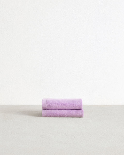 A set of two Bed Threads Violet 100% Cotton Terry Face Washers, soft and absorbent, are neatly folded on a light gray surface against a white background.