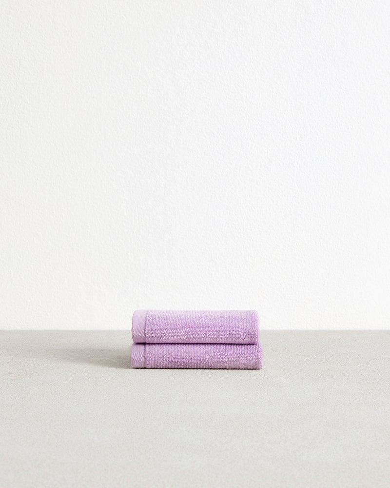 A set of two Bed Threads Violet 100% Cotton Terry Face Washers, soft and absorbent, are neatly folded on a light gray surface against a white background.