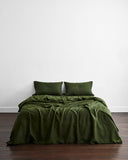 A neatly made bed features the Olive 100% French Flax Linen Duvet Cover and two matching pillows by Bed Threads, set against a white wall on wooden flooring, creating an inviting space with temperature-regulating bedding.
