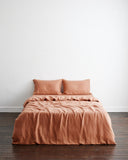 A neatly made bed features the Bed Threads Hazelnut 100% French Flax Linen Bedding Set—duvet cover and two matching pillows—set against a plain white wall and a dark wooden floor.